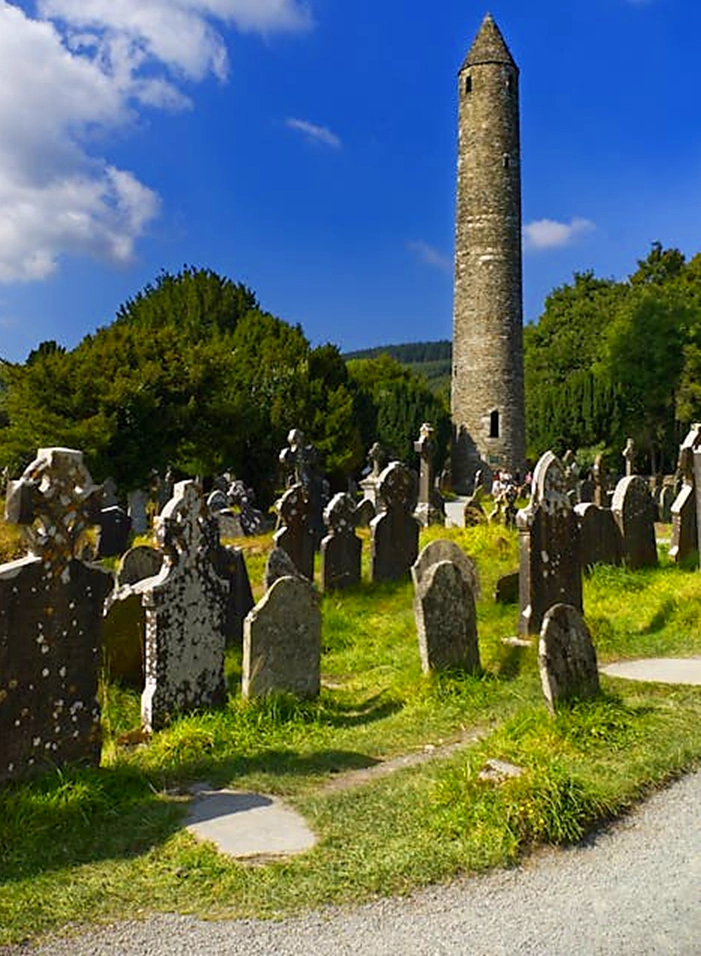 Round Tower at Glendalough with gravestones and celtic cross