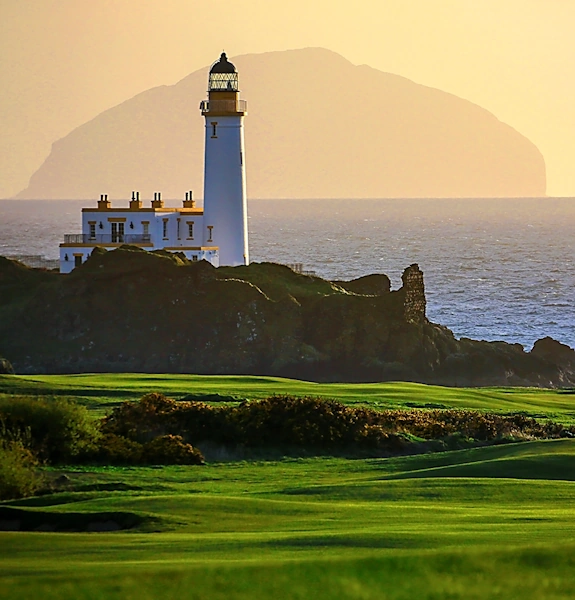 Stevenson lighthouse at Turnberry with big Ailsa Craig on the horizon against peach sky from the Robert the Bruce course