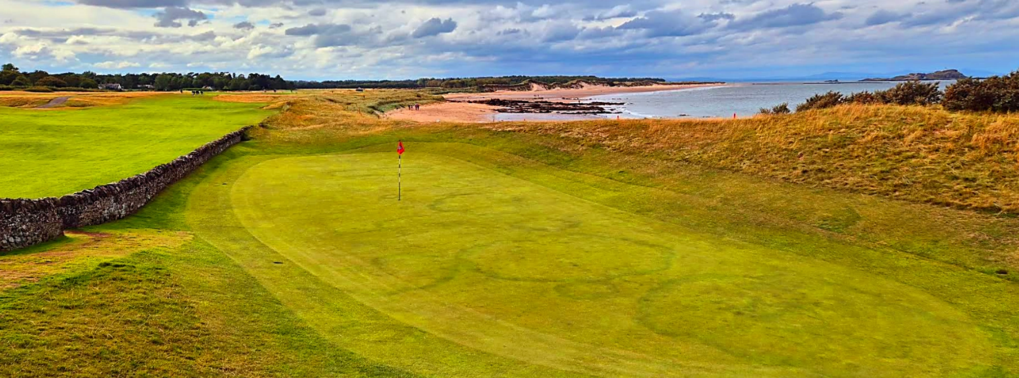 13th green at North Berwick with stonewall running down the left side separating the fairway and putting surface