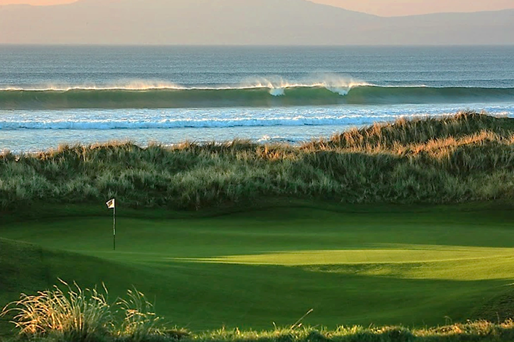 A green at Machrie golf club with a breaking wave in the background