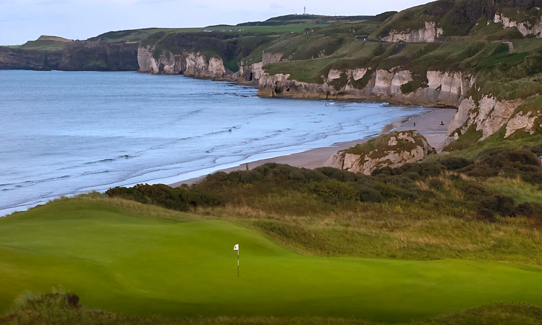 Portrush 5th green with cliffs, sea and beach below